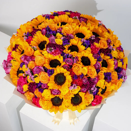 Vibrant Grand bouquet with golden sunflowers, orange and yellow roses, purple roses, fuchsia and purple carnations, pink statice, eucalyptus, and pistacia leaves, available for flower delivery in Lahore