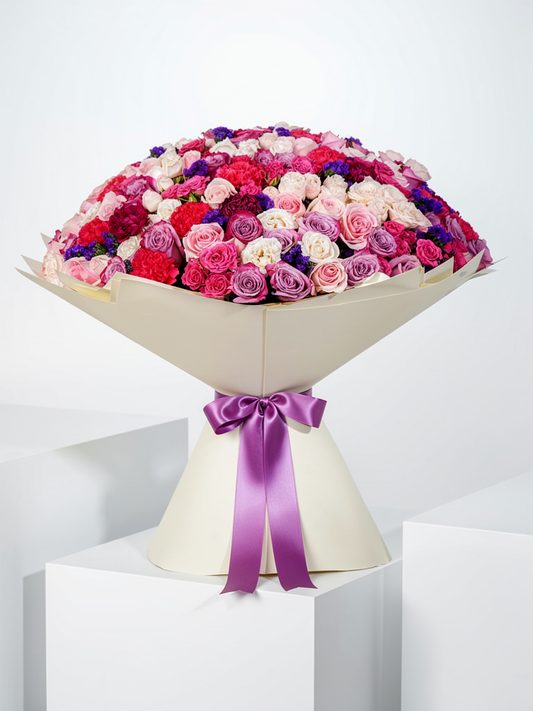Isabella Grand bouquet with Spray Rose Bombastic, purple statice, fuchsia and purple carnations, fuchsia roses, and deep purple roses, wrapped in signature Grand style, available for flower delivery in Lahore