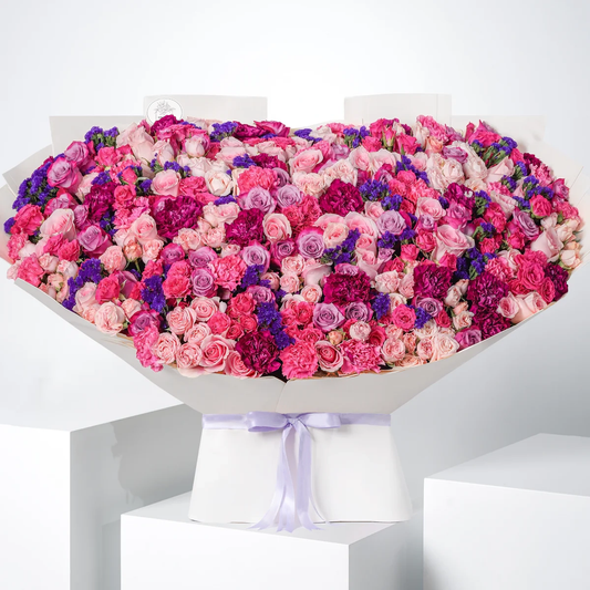 Isabella Grand bouquet with Spray Rose Bombastic, purple statice, fuchsia and purple carnations, fuchsia roses, and deep purple roses, wrapped in signature Grand style, available for flower delivery in Lahore