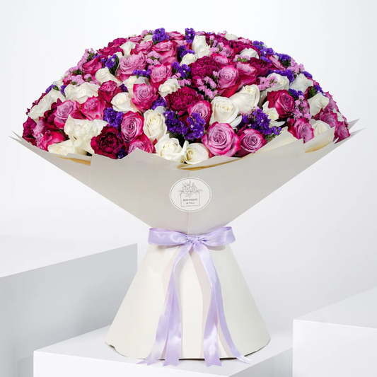 Ivy Grand bouquet with purple and white roses, purple carnations, and pink and purple statice, wrapped in elegant Grand wrap, available for flower delivery in Lahore