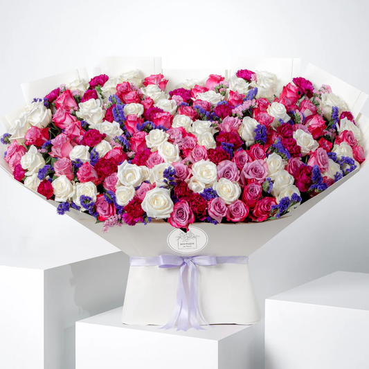 Ivy Grand bouquet with purple and white roses, purple carnations, and pink and purple statice, wrapped in elegant Grand wrap, available for flower delivery in Lahore