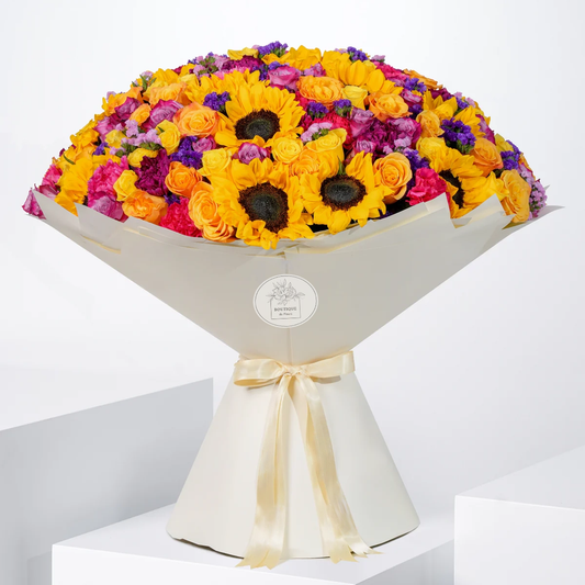 Vibrant Grand bouquet with golden sunflowers, orange and yellow roses, purple roses, fuchsia and purple carnations, pink statice, eucalyptus, and pistacia leaves, available for flower delivery in Lahore